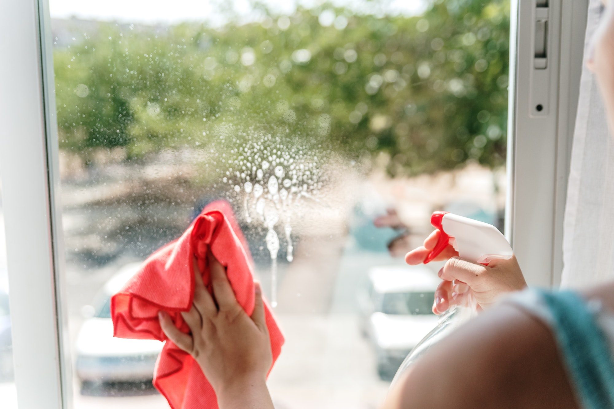 Woman's hand cleaning a window pane with a cloth and window cleaning liquid.