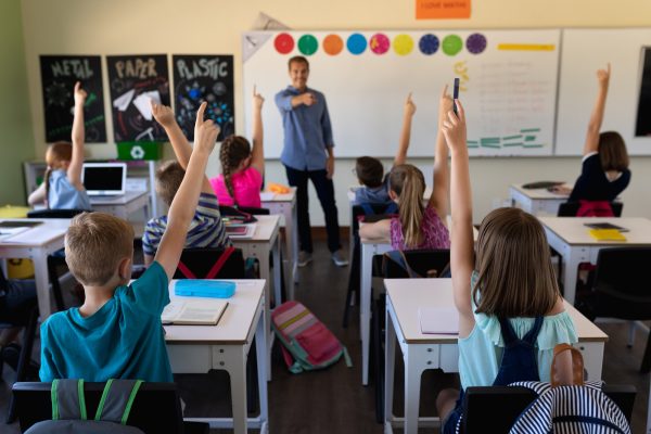 Male school teacher standing in an elementary school classroom with a group of school children