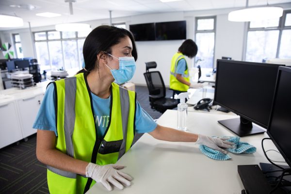 Woman wearing hi vis vest and face mask cleaning the office using disinfectant